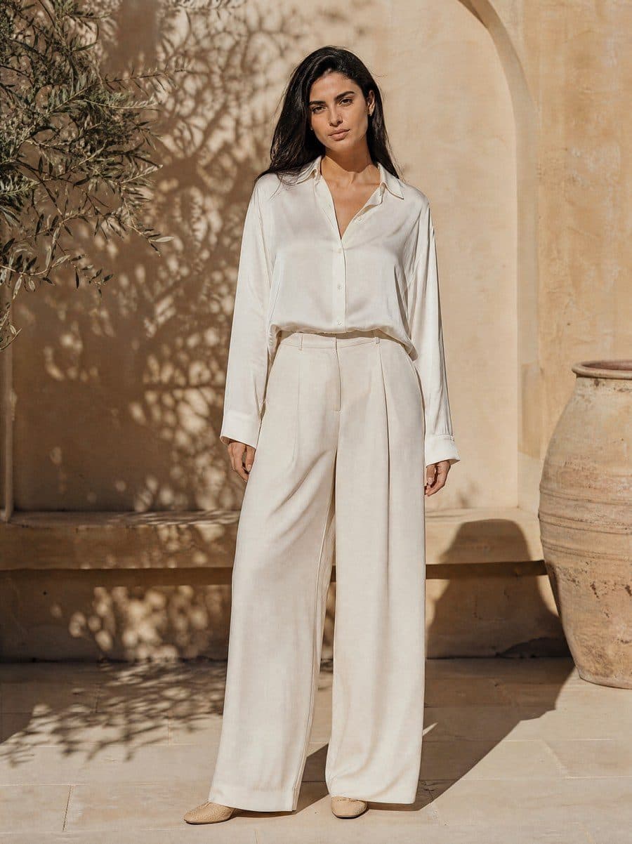 Model in a white satin blouse and wide trousers in a sunlit courtyard, the original photo